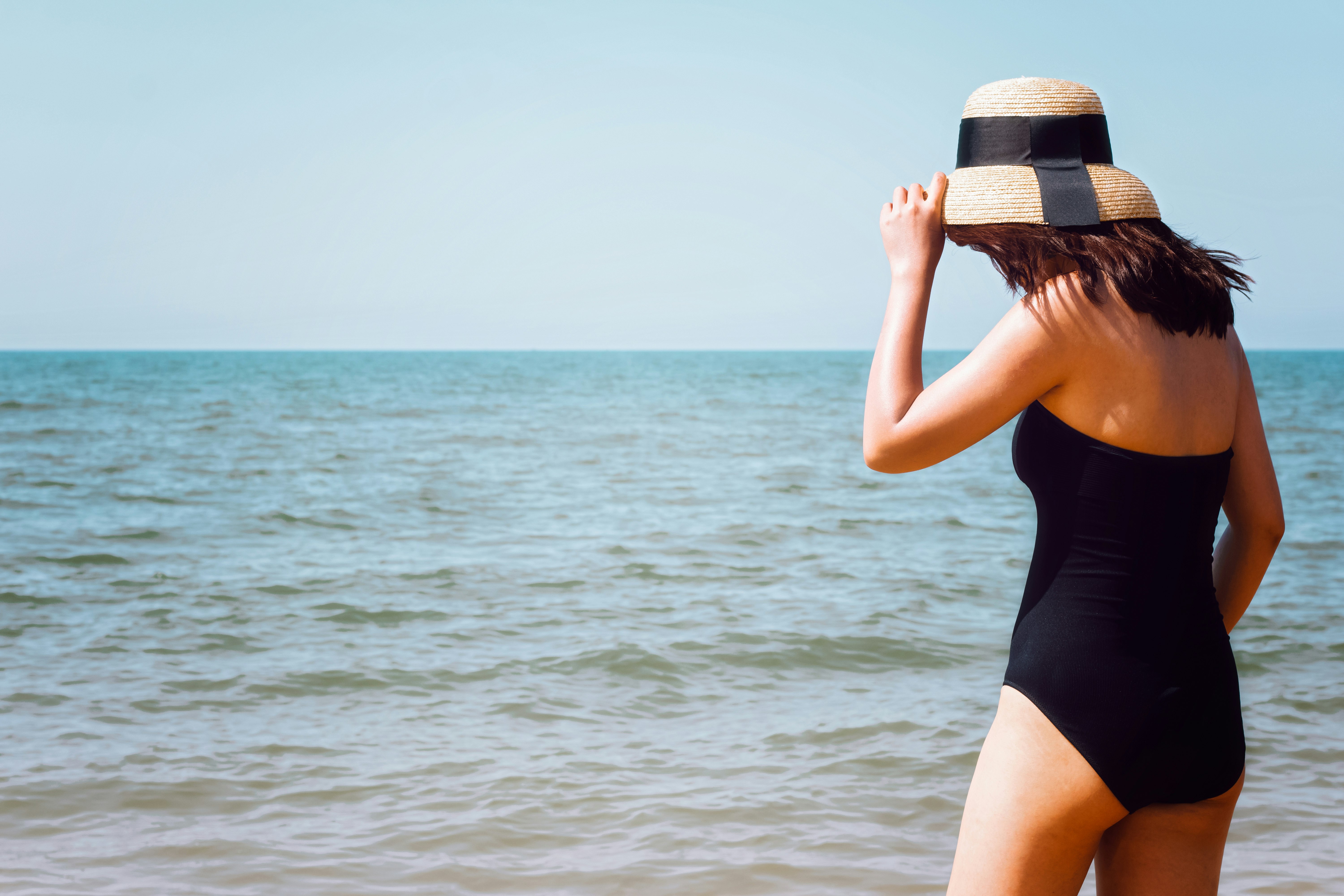 woman wearing black onepiece swimsuit standing beside seashore at daytime